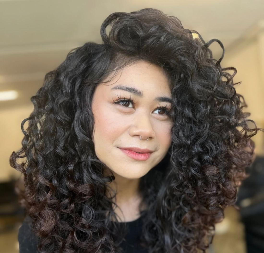 A client smiling with a full head of defined, voluminous dark curls after her appointment