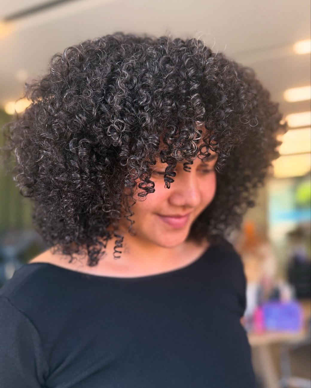 Tight dark curls threaded with natural silver, freshly shaped in the warm light of the studio